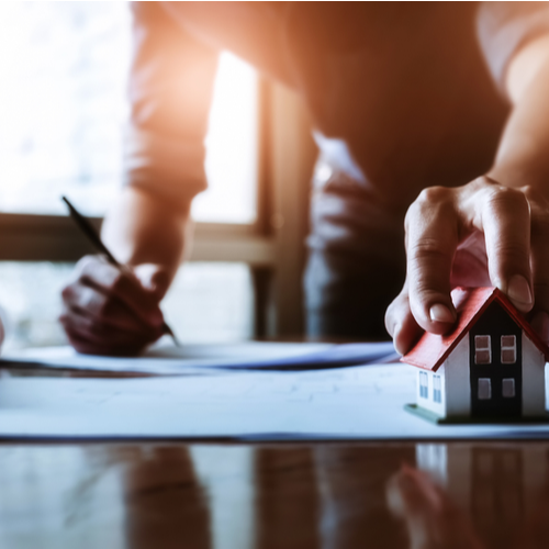 Person signing papers beside a small house model on a desk