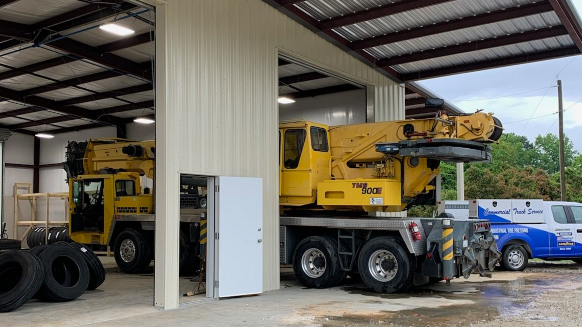 Yellow crane inside a metal building, with tires and a white van.