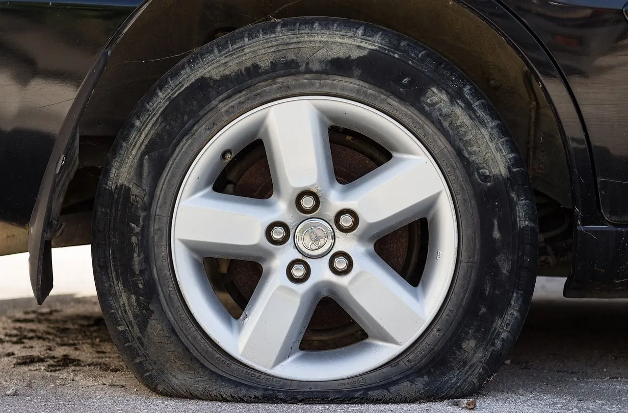 Flat car tire on a black car; silver rim, tire deflated.