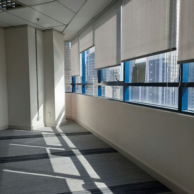 Empty office hallway with sunlight through windows and blinds casting shadows on the carpet