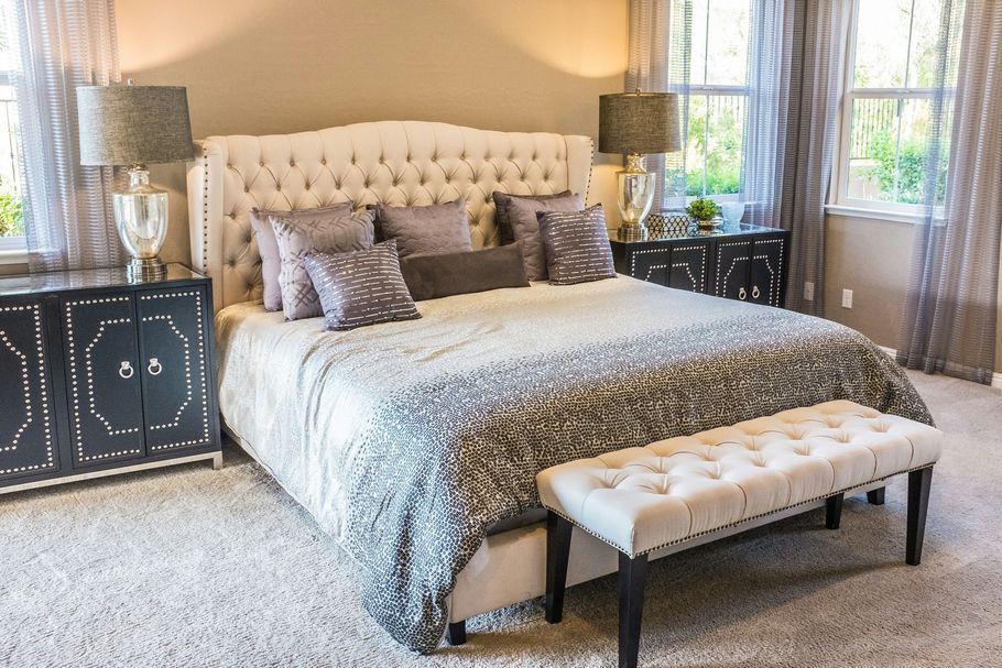 Elegant bedroom with tufted cream bed, gray bedding, mirrored nightstands, and a bench at the foot of the bed