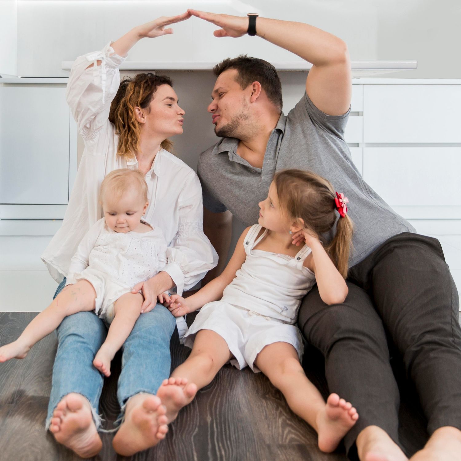 Family making a roof with their arms; two children, parents kissing, sitting on floor.