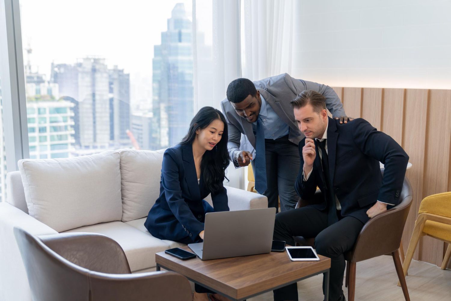 Three business professionals looking at a laptop in an office setting.