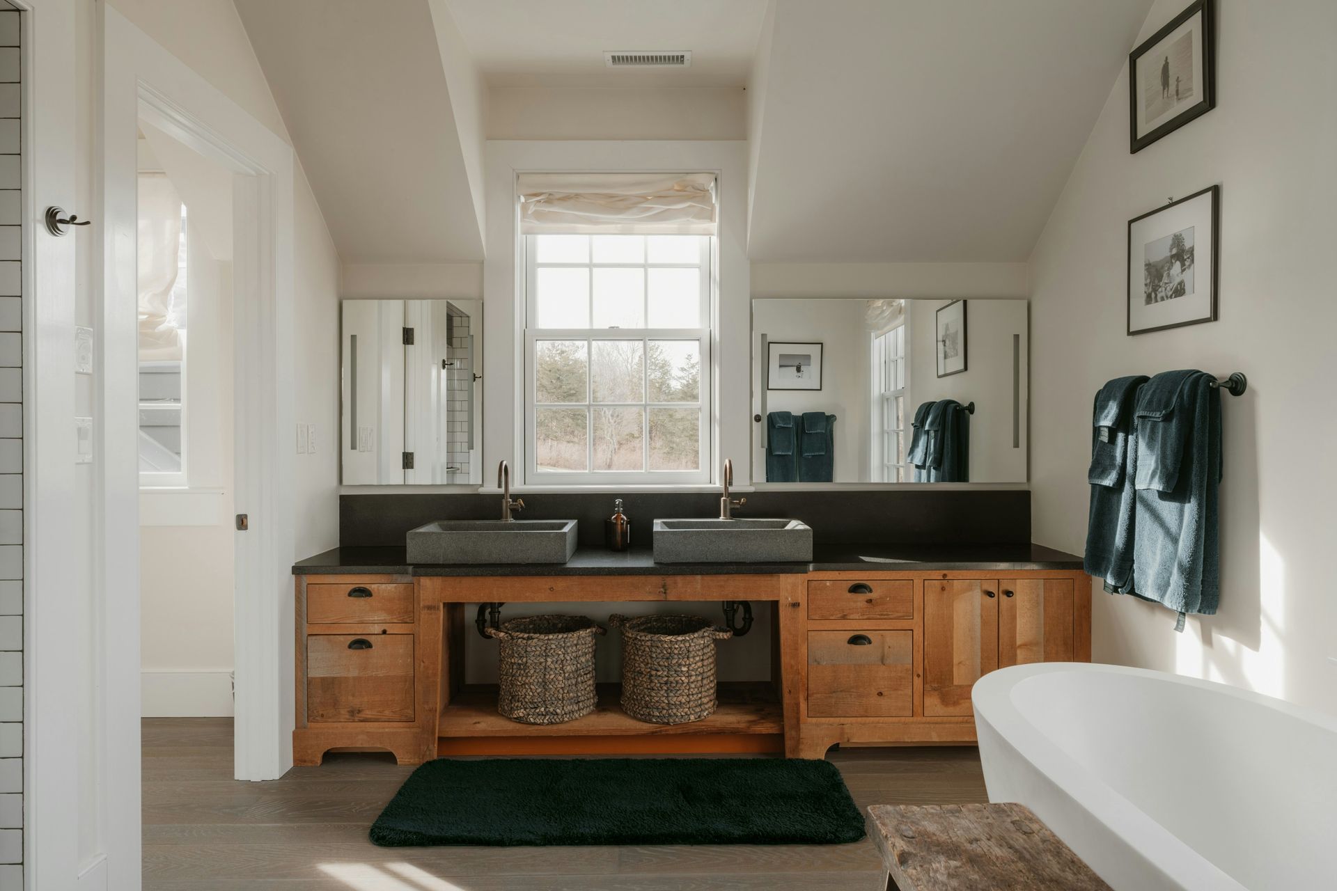 Modern bathroom with double vanity, large mirror, bathtub, and window with blinds