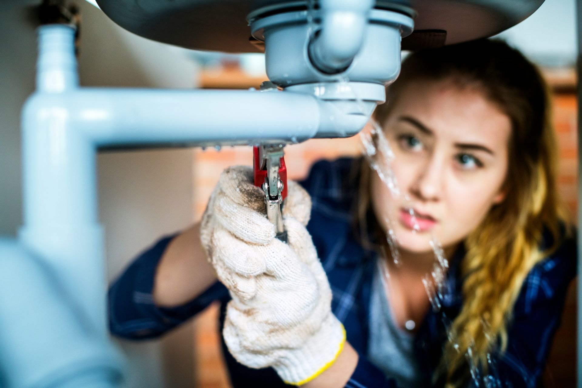 Person repairing plumbing under a sink with a wrench, wearing gloves, in a close-up indoor scene
