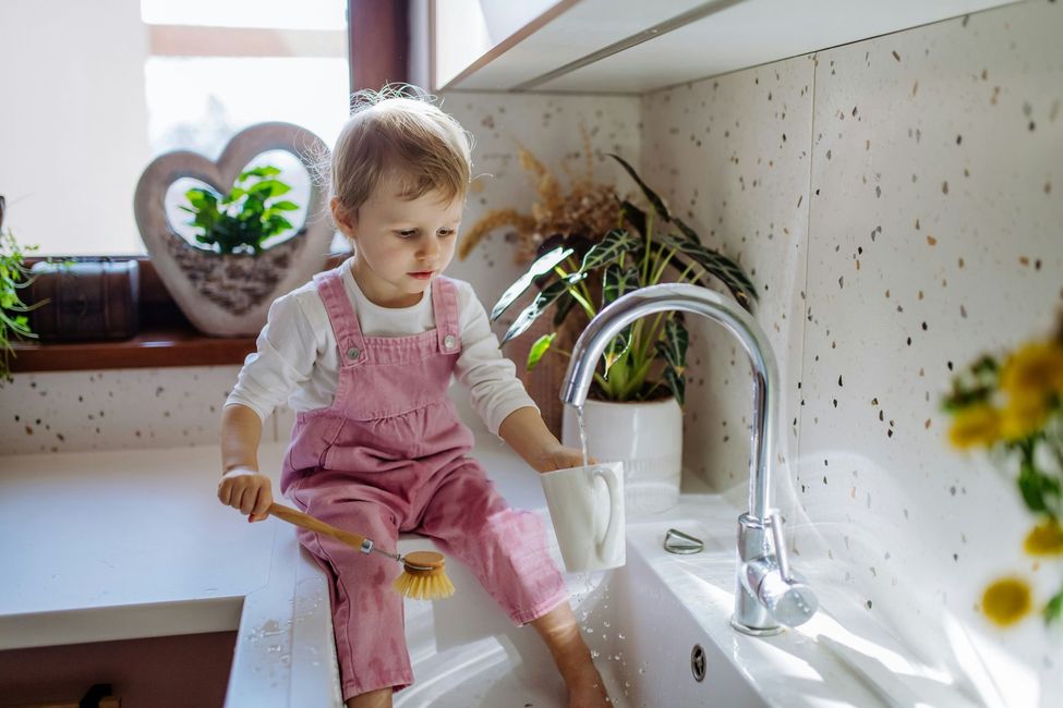 Hand turns faucet on, water splashes into a glass in a kitchen sink.