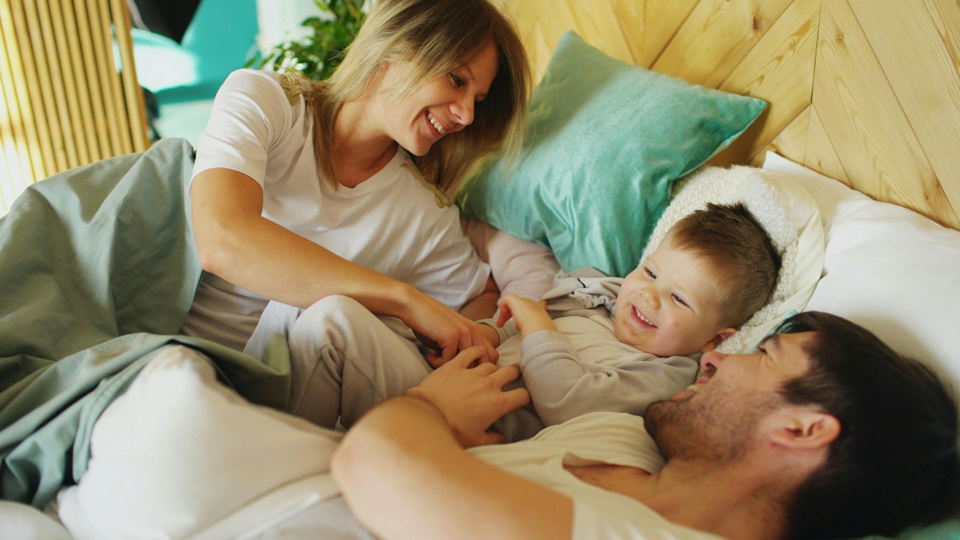 Family lying on a bed, smiling and tickling a child in a cozy bedroom.
