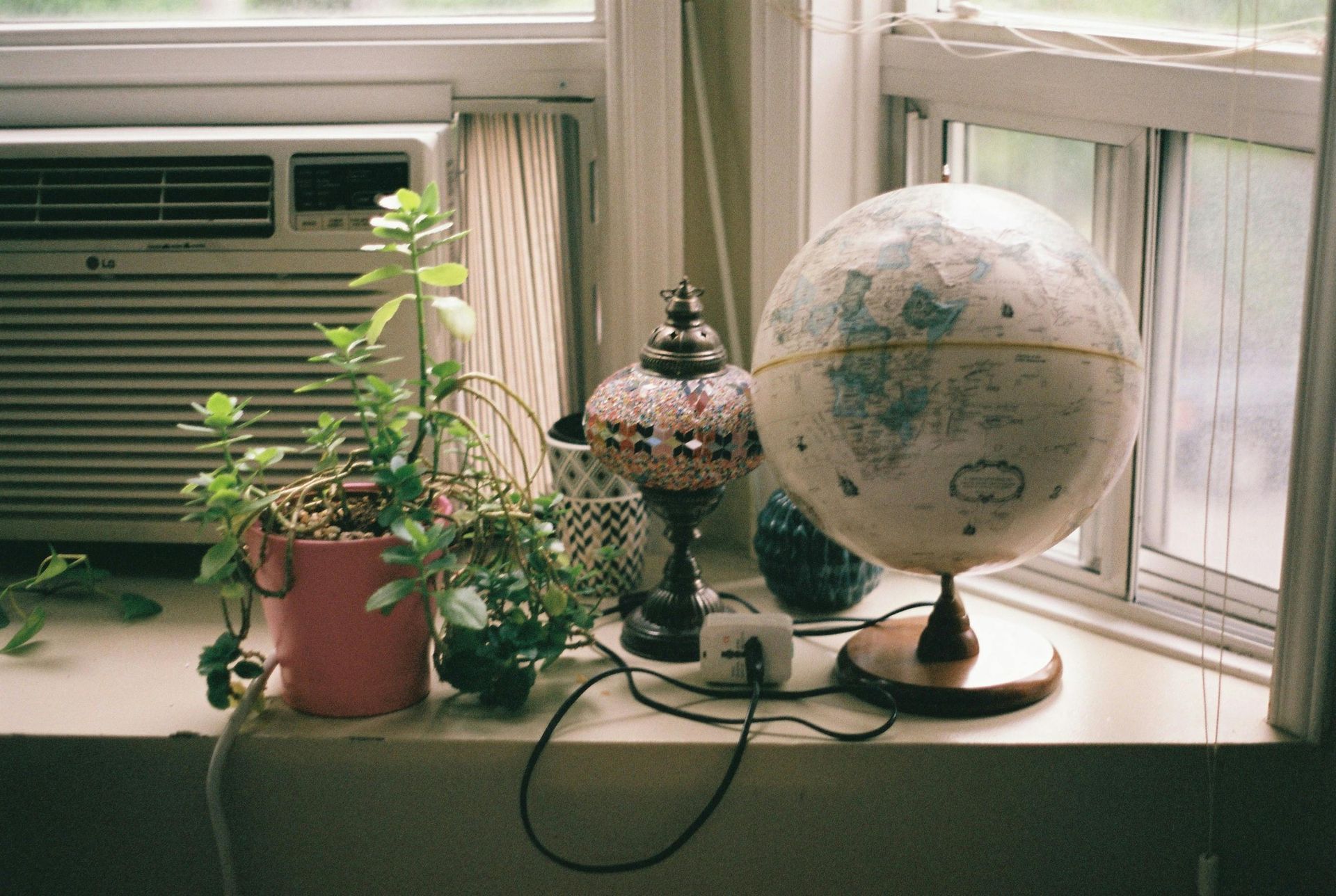 Potted plant, decorative lamp, and globe on a windowsill beside an air conditioner