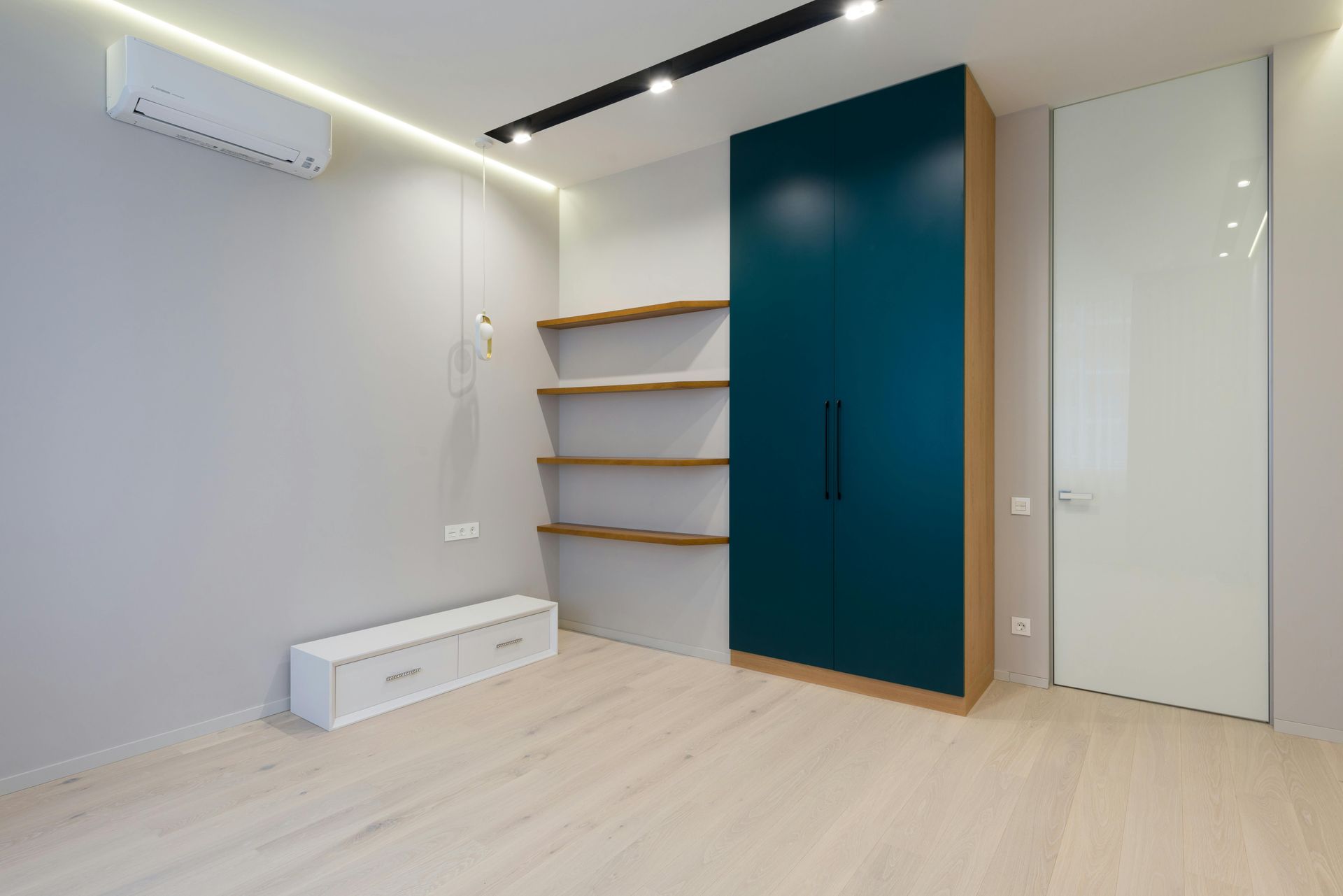 Empty modern room with light wood floor, wall shelves, teal wardrobe, and white sliding closet door