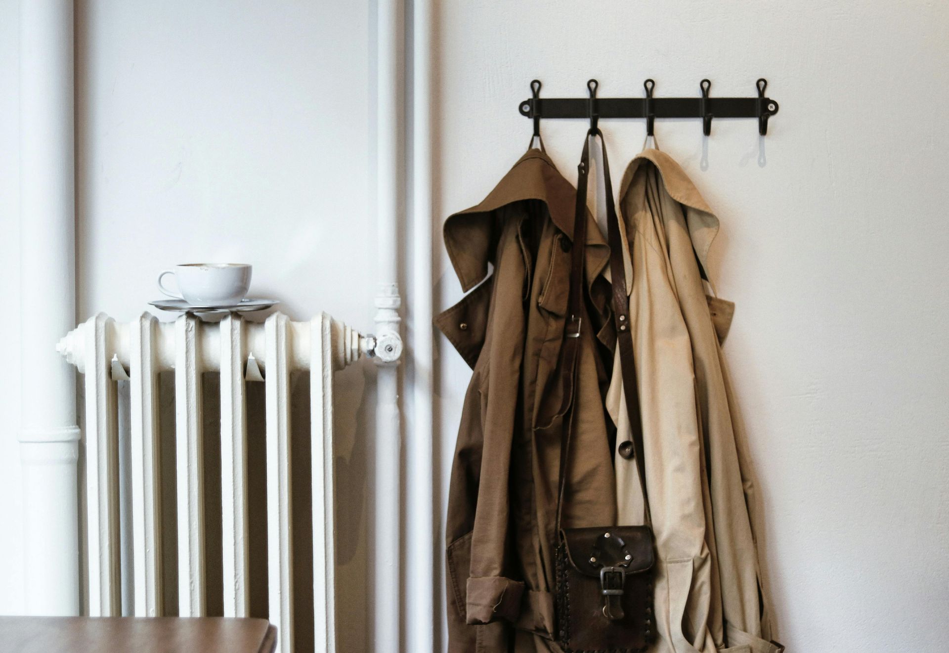 Coats hanging on wall hooks beside a white radiator in a minimalist room