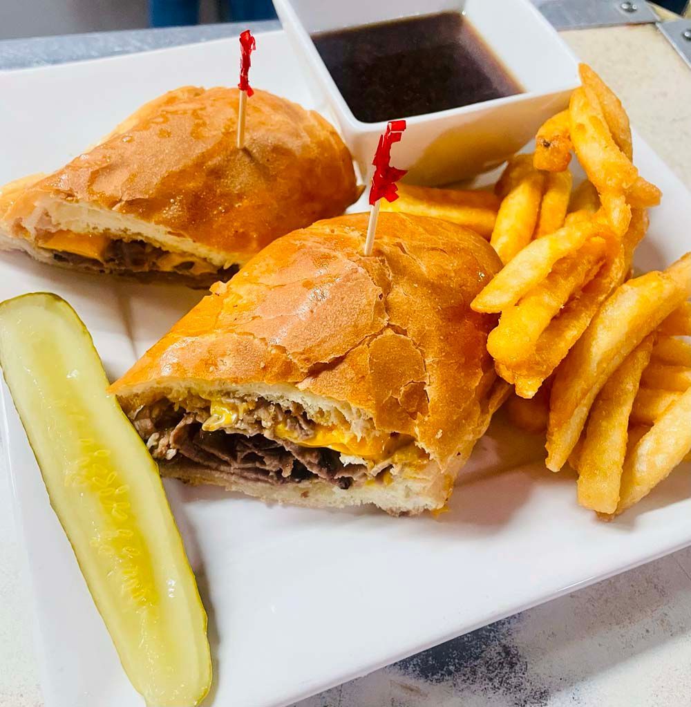 A sandwich with french fries and a pickle on a white plate.