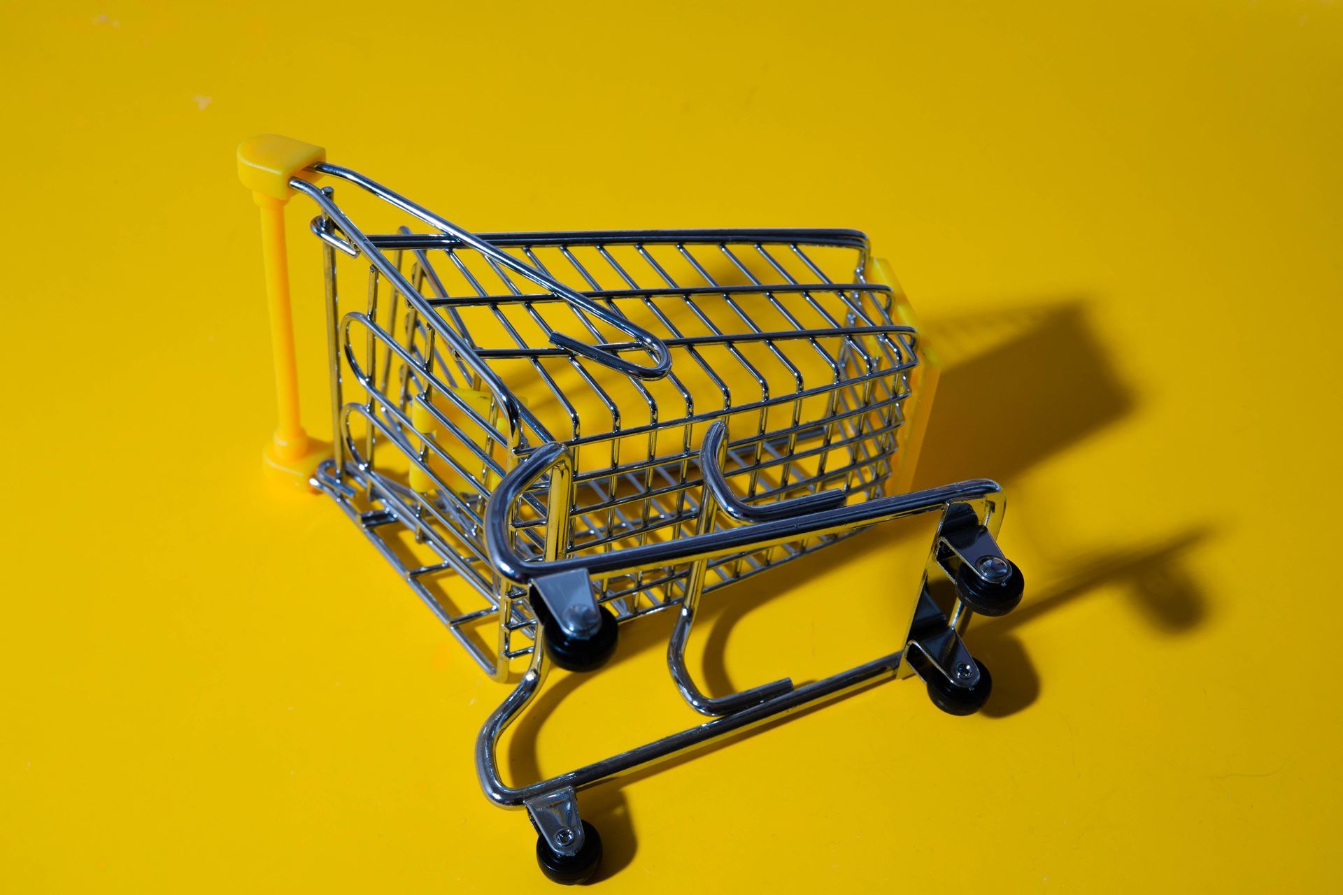 Small silver shopping cart on a bright yellow background