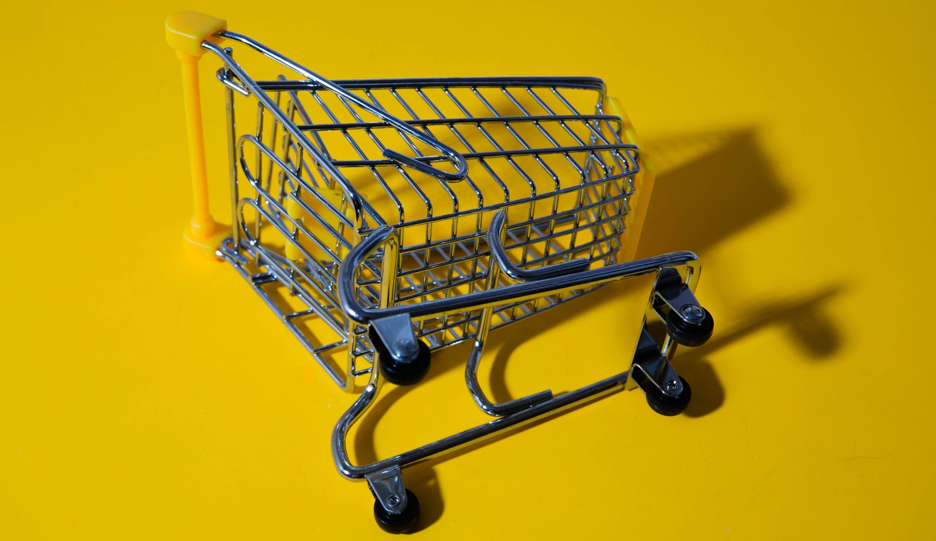 Mini shopping cart with blue wheels on a bright yellow background, casting a shadow