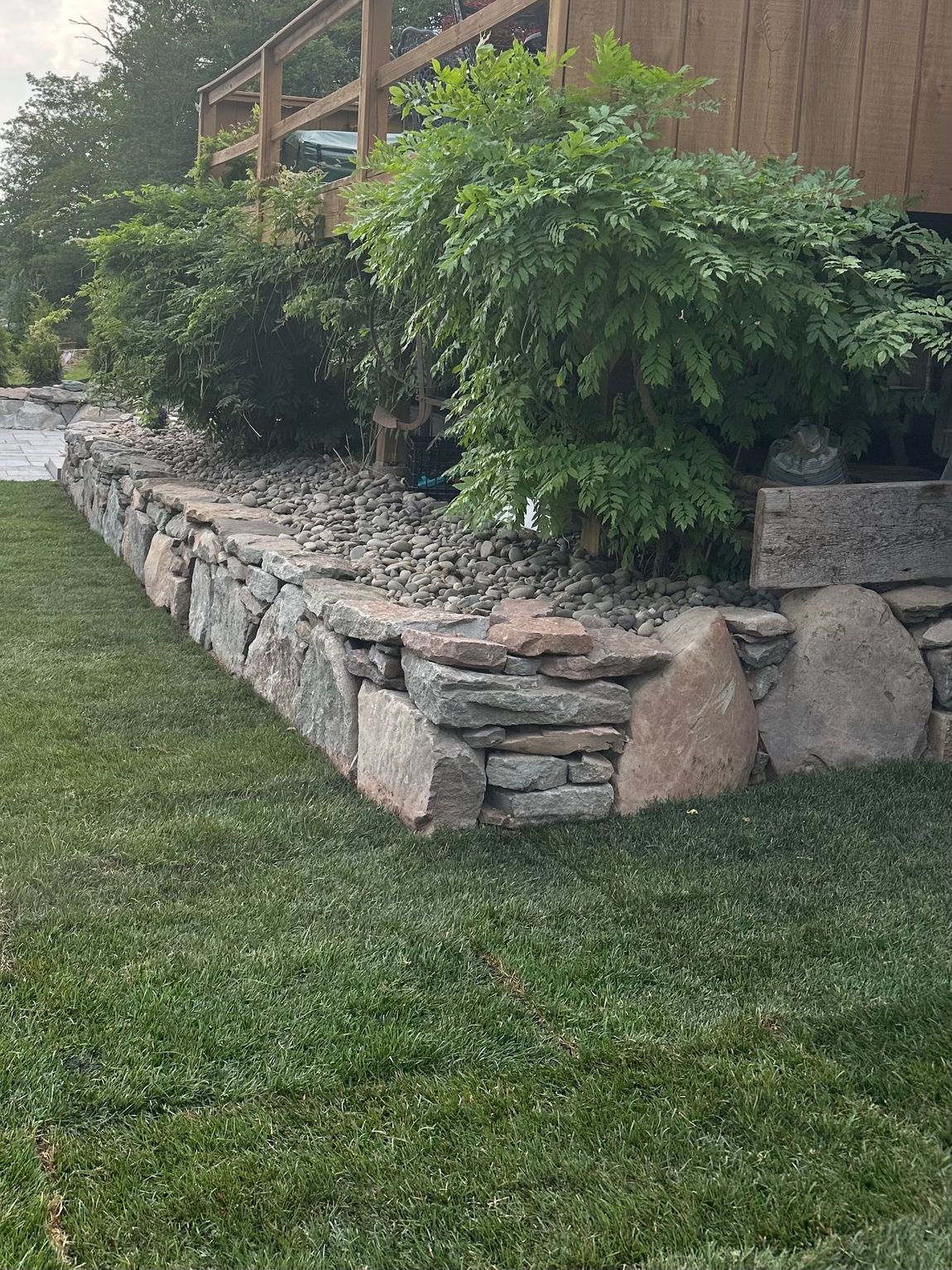 A large rock is sitting in the middle of a dirt field in front of a house.