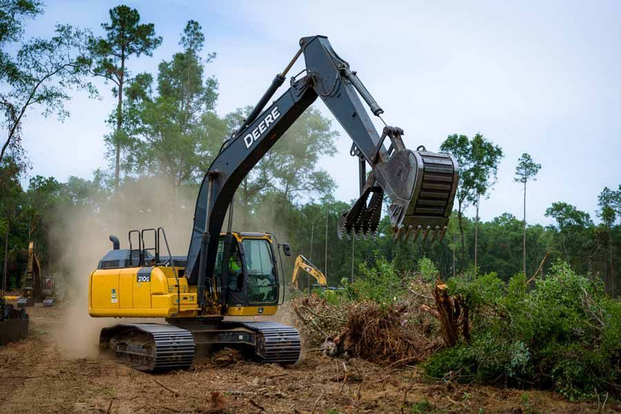 A large yellow excavator is driving through a forest.