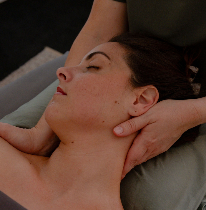 Person lying face down while receiving a neck and shoulder massage on a gray pillow