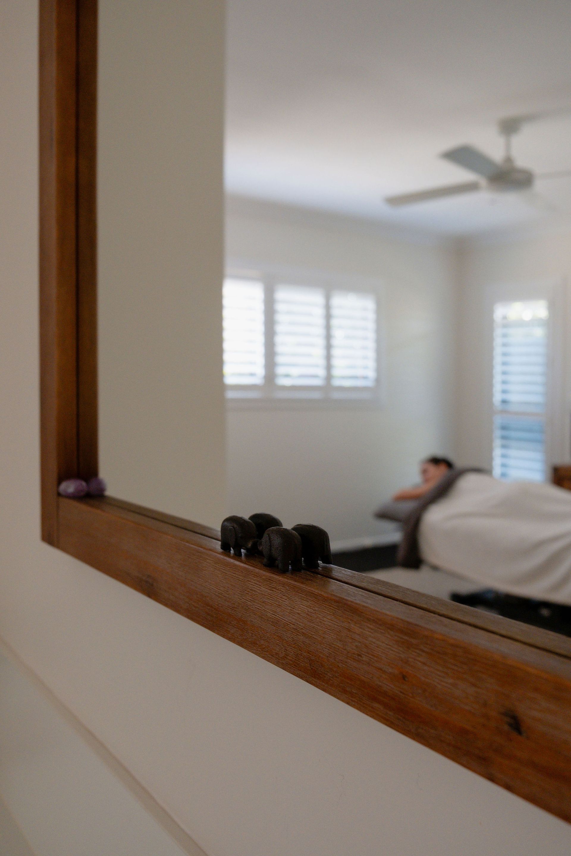 Bedroom reflected in a wooden-framed mirror, showing a person lying on a bed and a ceiling fan.