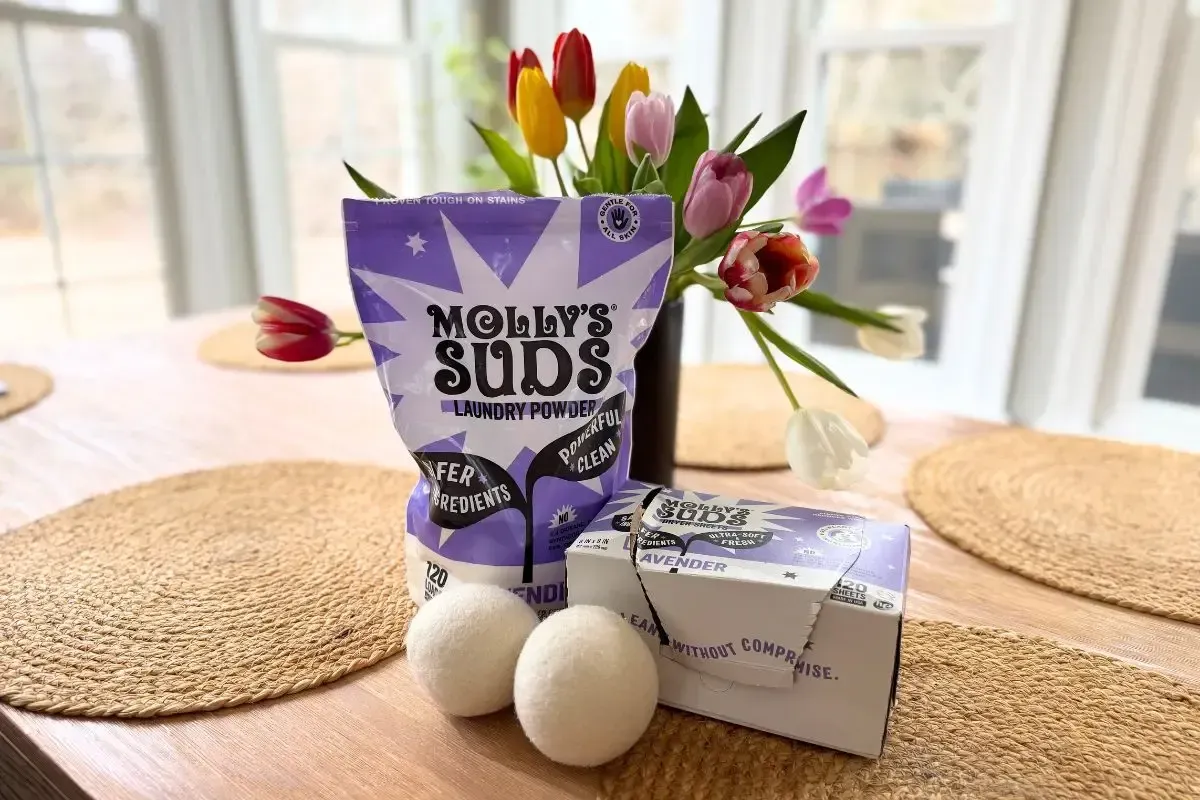 Molly's Suds laundry detergent, dryer sheets, and wool dryer balls on a table in front of flowers