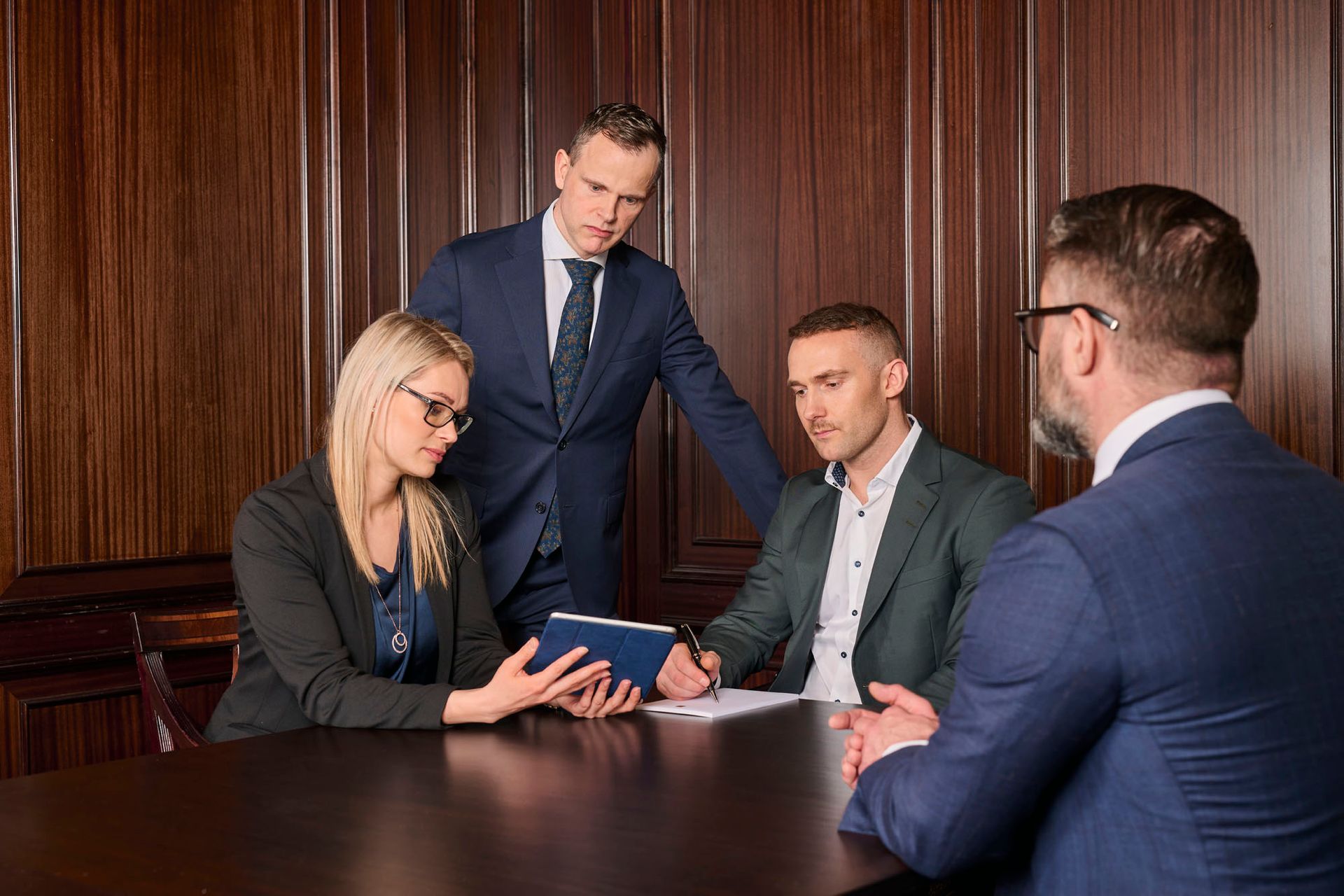 Hópur viðskiptamanna situr við borð og horfir á spjaldtölvu.