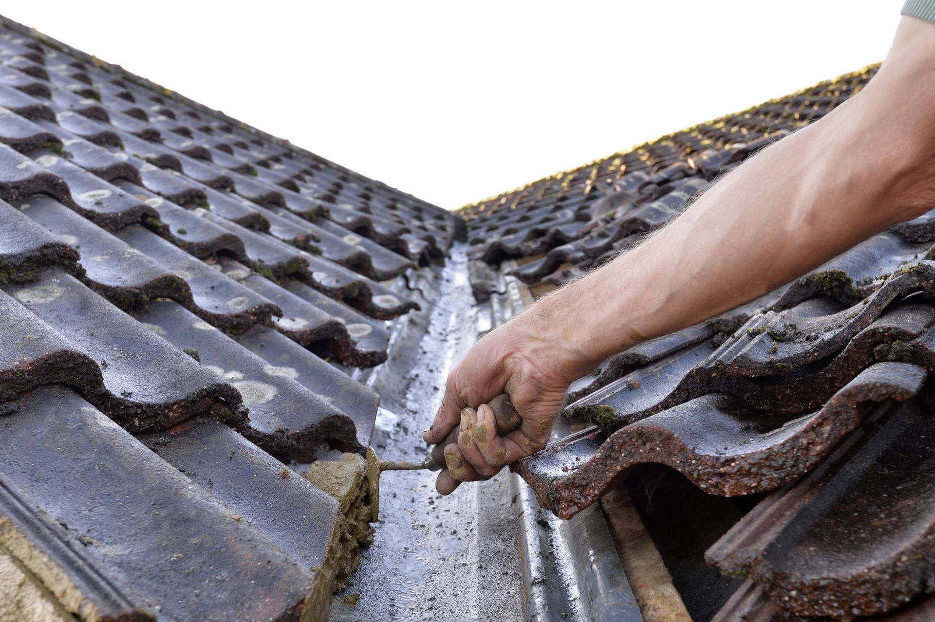 A person is working on a tiled roof with a hammer.