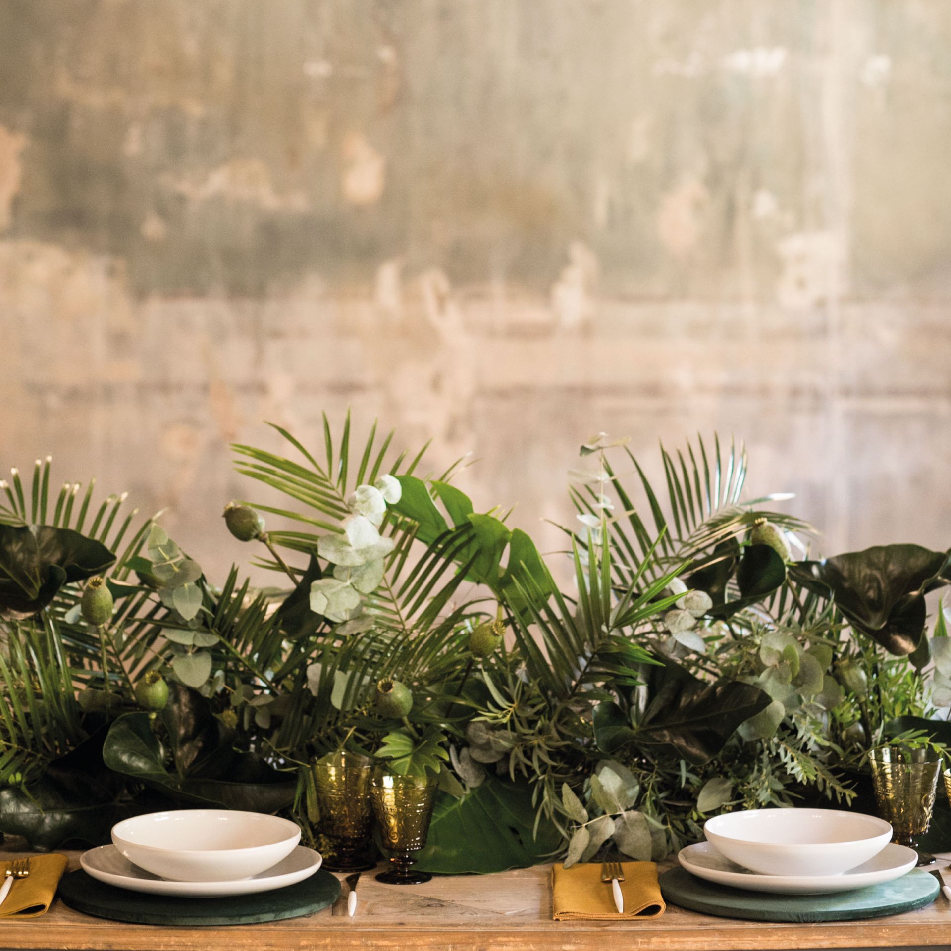 a table with plates and glasses surrounded by green plants