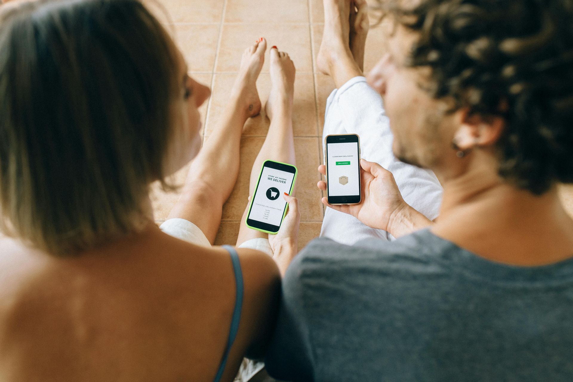 A man and a woman are sitting on the floor looking at their phones.