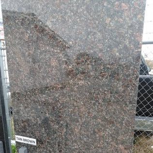 Dark brown polished stone slab with a small label, displayed outdoors by a fence.