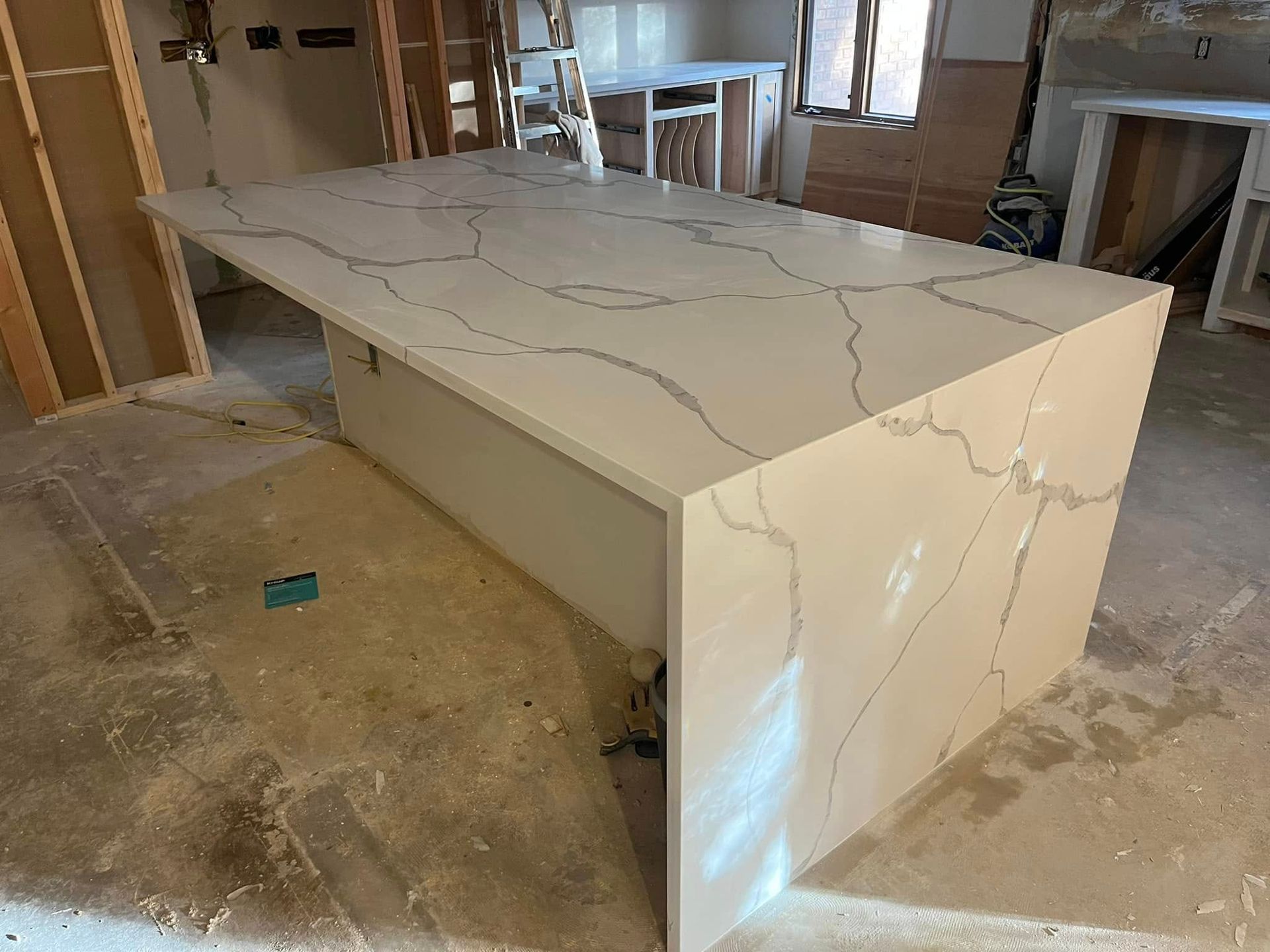 Large white stone kitchen island with gray veining in an unfinished room