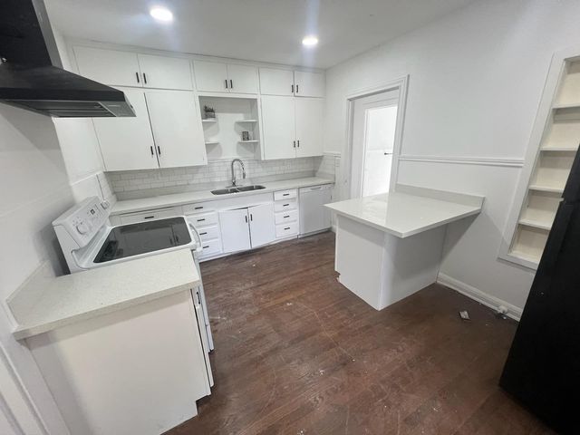 Bright white kitchen with dark wood floor, island, sink, stove, and open shelving