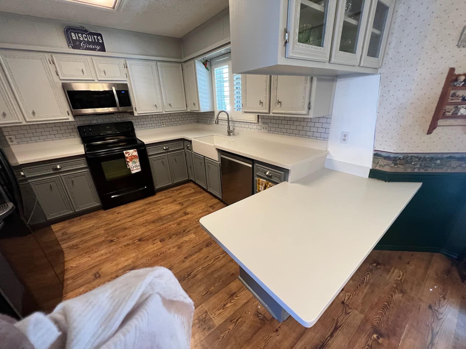 Bright kitchen with white cabinets, black stove, wood floor, and a white countertop peninsula