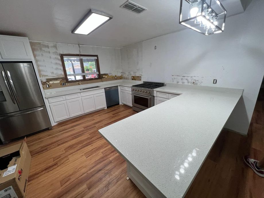 Bright kitchen with white counters, wood floors, stainless fridge, and a large island under pendant lights