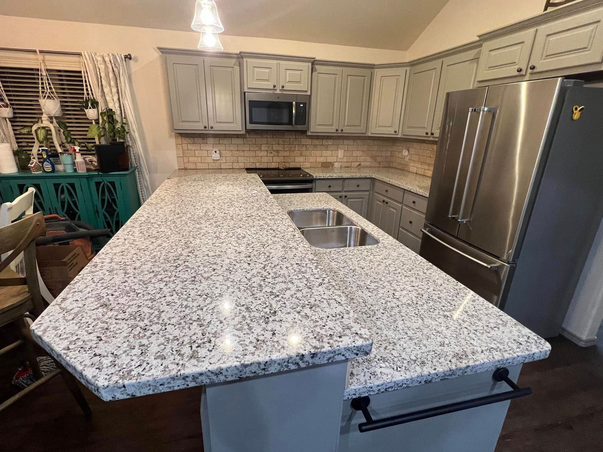 Modern kitchen with a granite island, gray cabinets, stainless steel appliances, and a tiled backsplash