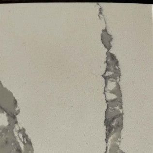 Cracked white wall with vertical peeling plaster exposing gray material
