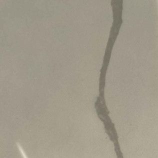 Close-up of a gray crack running vertically on a beige wall.