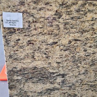 Close-up of beige granite slab with dark speckles and a small white label in the upper left corner