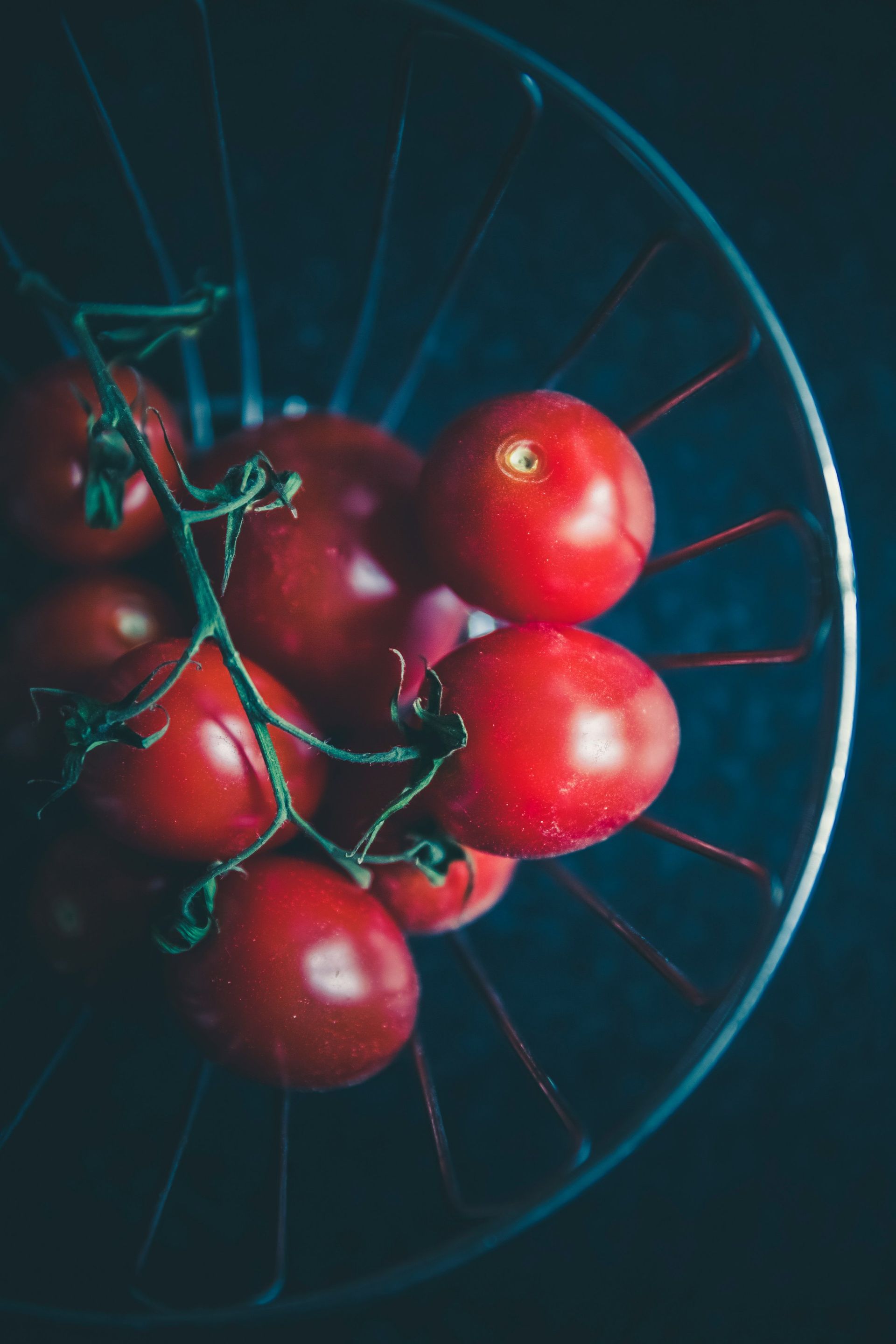 A glass bowl filled with red tomatoes on a vine.