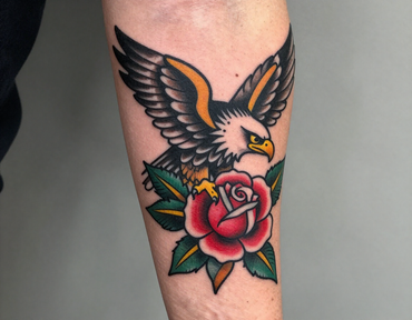 Eagle tattoo above a red rose with green leaves on a forearm