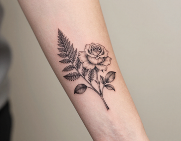 Black floral tattoo of a rose and fern on a forearm