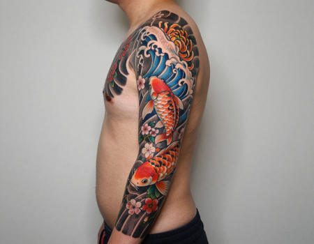 Side view of a person showing a colorful koi and wave tattoo sleeve on the arm and shoulder
