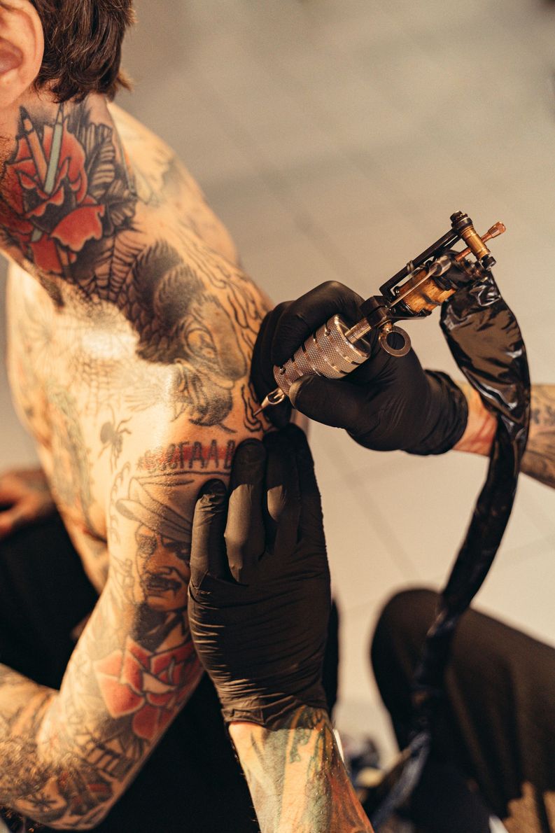 Tattoo artist using black gloves applies ink with a tattoo machine on a client’s arm
