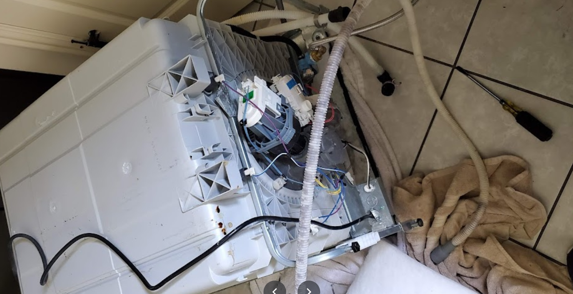 A broken washing machine is sitting on the floor next to a screwdriver.