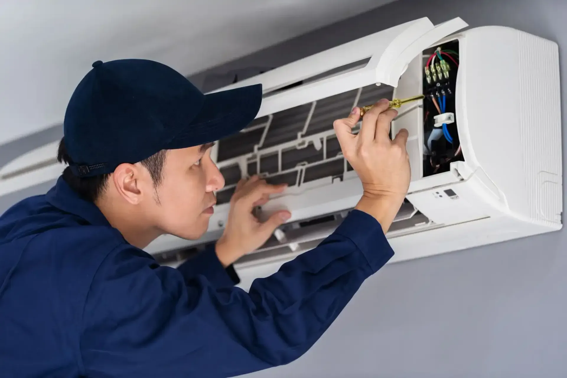 Person cleaning an air conditioner with a vacuum nozzle.