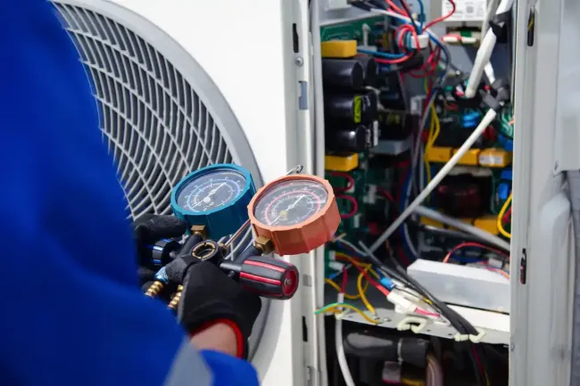 HVAC technician using gauges on an air conditioning unit for maintenance. Close-up on machinery.