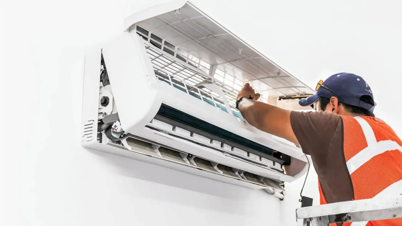 HVAC technician installing an air conditioning unit on a white wall.