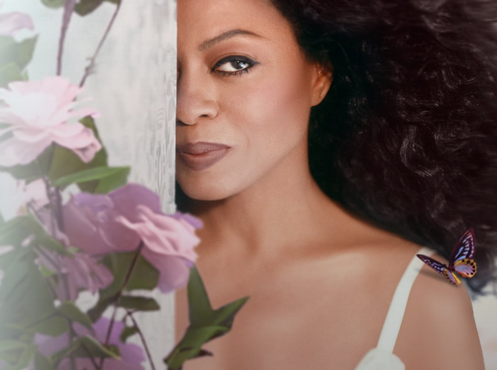 Woman partly behind pink flowers, with dark hair and a butterfly on her shoulder.