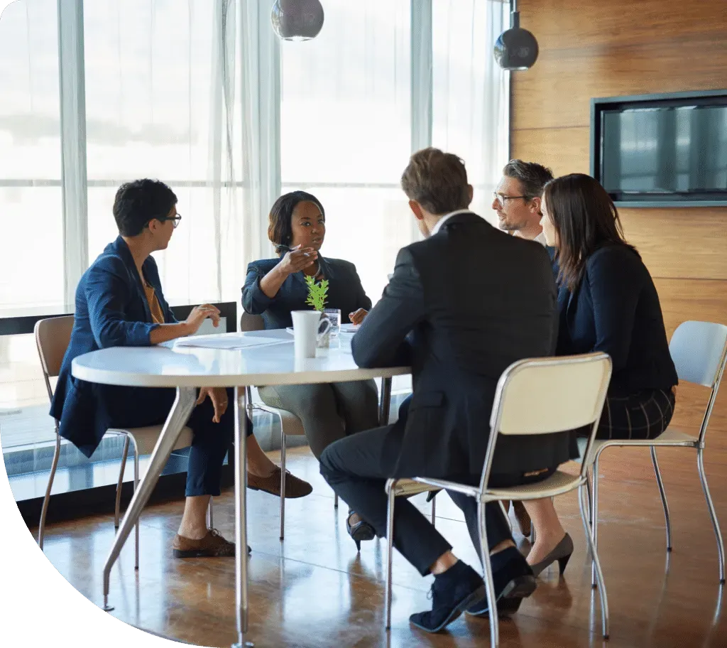 People at a round table meeting in a modern office with natural light, discussing.