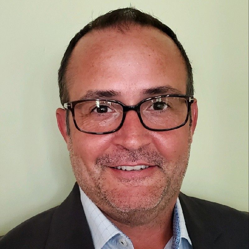 Man in glasses and dark blazer smiling against a pale green background