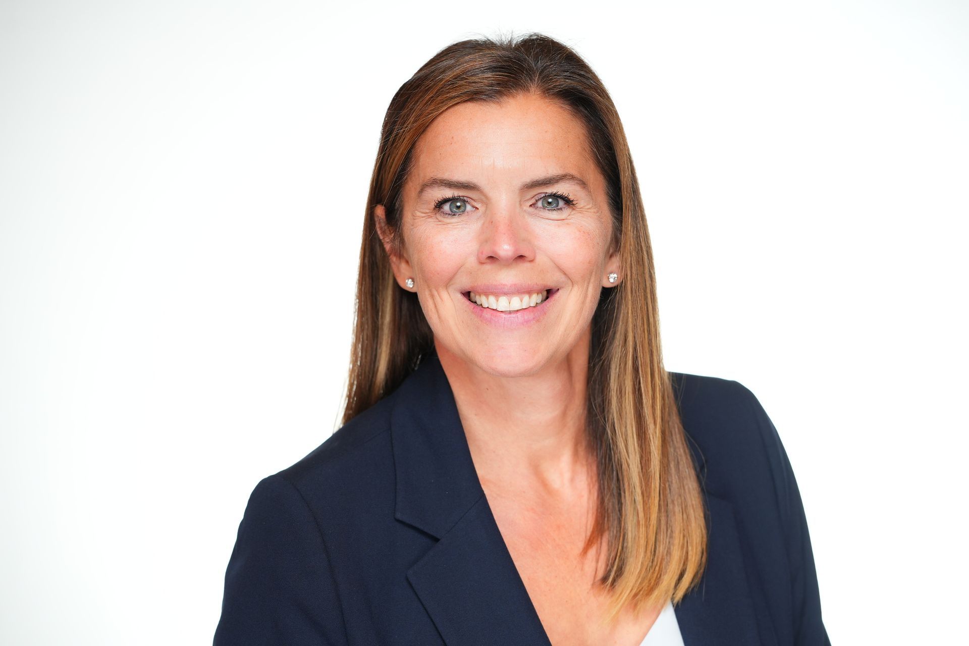 Woman with brown hair smiling, wearing a black blazer and green top, against a dark gray background.