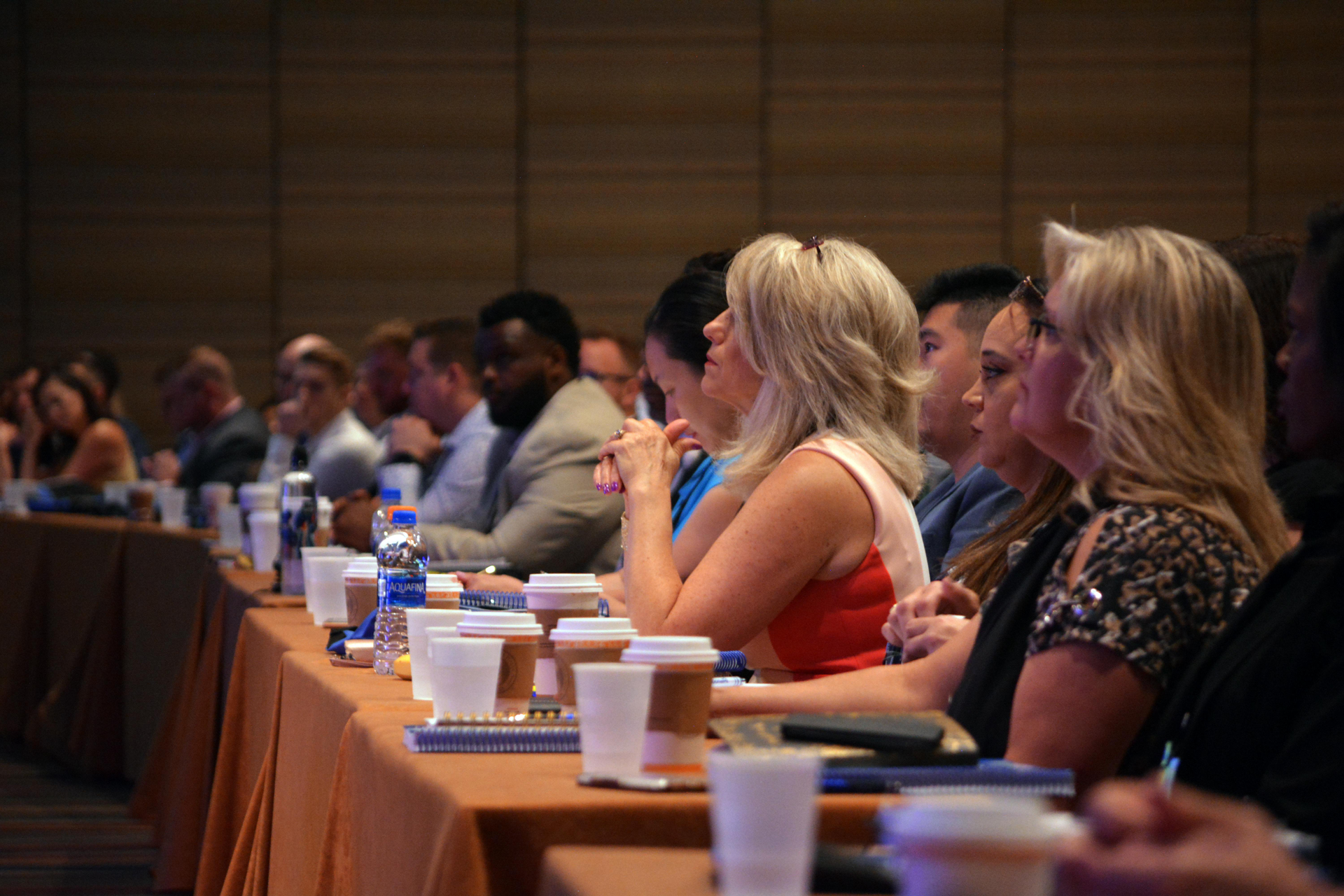 Attendees at a conference seated at a long table, listening intently.