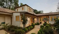 A low-angle view of a modern Mediterranean-style home with cream stucco walls, a tile roof, and a landscaped courtyard.